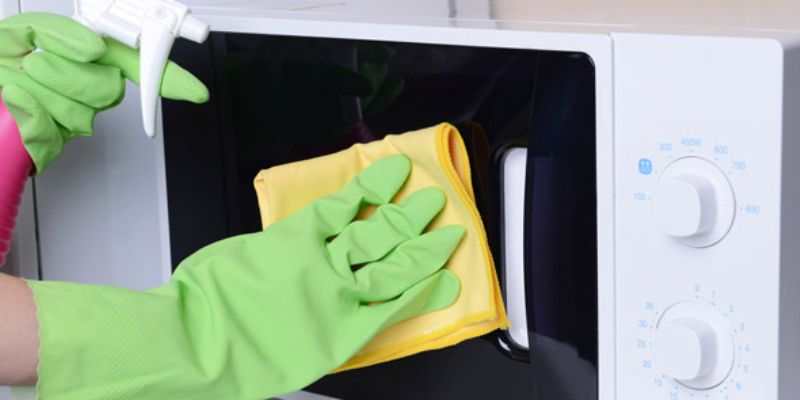 A person cleaning the door of a microwave
